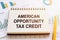 AMERICAN OPPORTUNITY TAX CREDIT - written on notepad on financial charts and graphs with yellow pen