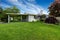 American rambler exterior. Grass filled yard with shrubs.