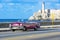 American red purple 1955 convertible vintage car on the promenade Malecon and in the background the Castillo de los Tres Reyes del