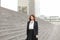 American secretary standing on stairs with bag and high buildings in background.