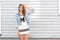 American stylish young woman in a summer blue denim jacket in a sporty white dress in black print poses