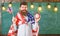American teacher with american flags holds alarm clock. Man with beard on cheerful face holds flag of USA and clock