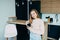 American teenage girl at Home kitchen interior holding Black coffee cup. Woman in pink blouse and blue jeans lean on wooden counte