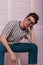 American young man hipster in fashionable glasses in a striped stylish t-shirt in trendy jeans is resting on a chair near a wooden