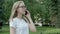 Amiable youthful woman in spectacles answering briefly on a phone call spending time outside on sunny summer day. Camera