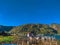 Amidst rolling hills, a serene lake reflects the clear blue sky, while a charming house nestles at the base of the hills.