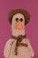 Amigurumi duck doll on pink background. Soft DIY toy made of cotton. One brown goose with orange beak wears hat and