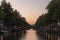 Amsterdam canal and bridge, at dusk. The canal is calm and the lights around the bridges arches are reflecting on the water