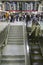 Amtrak train travelers stand in line under Departures sign, while a man goes down escalator at Penn Station, New York City