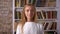 Amused caucasian blonde woman is standing straight and looking at camera with chill face on books background isolated
