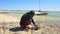 Anakao, Madagascar - May 03, 2019: Local Malagasy fisherman cutting freshly caught pufferfish with knife, crouching at sandy beach