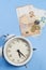 Analog classic alarm clock on a blue wooden background with euro bills and cents