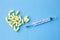 Analog thermometer on blue background with bunch of medicaments in white/yellow capsules