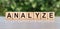 Analyze word written on wooden blocks. The text is written in black letters and is reflected in the mirror surface of the table.