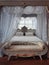 Ancient bedroom furniture style, medieval king bed, near the window, white curtains canopy and gold details. Close up background