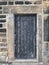 Ancient black wooden door with old faded peeling paint in a heavy stone frame with a closed bolt and metal hinges