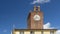 The ancient clock tower in the historic center of Cascina, Pisa, Italy, against a beautiful blue sky with white clouds