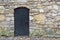 An ancient door in black with a large lattice texture with large rivets against the background of a wall and a non-hewn granite st