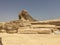 Ancient Egyptian sphinx made of yellow stone against the background of the mighty pyramids of the great Phraon Cheops.
