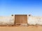 Ancient Egyptian wooden door with old white cement wall under blue sky. Oasis and Berber constructions in the desert