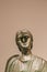 Ancient Greek brass sculpture of woman with a bashed in face against tan background - room for copy