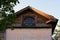 Ancient house with oval window in the attic against blue sky. Vintage house with roof decorated by the carved wooden platbands.