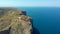 Ancient lighthouse up on the rock, located on the edge of green rocky mountain cliff and seascape breathtaking aerial drone point