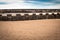 Ancient medieval fortress barrier wall on sandy beach as breakwater, in sunny blue sky with clouds, creative background design