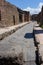 Ancient ruin street with two tourists in Pompeii, Italy. Antique road in italian ancient town. Pompeii landmark.