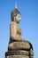 Ancient sculpture of a seated Buddha close-up against a blue sky. Sukhothai, Thailand