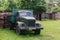 Ancient Soviet car in green meadow and old abandoned wooden outdoor toilet in the countryside of Latvia