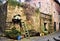 Ancient stone wall of a low building with a small balustrade and some iron containers painted in Barga.