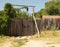 Ancient wooden gate with fence made of logs. Entrance to country courtyard in field.