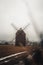 Ancient wooden mill standing alone in a field in gloomy foggy weather. Historical building for grinding corn, Opava, Czech