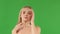 Angel blonde girl with perfectly smooth skin touching her face with her hands on an isolated green background. Perfect