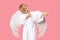 Angel Cherub child boy with large white wings is aiming at man to make him fall in love. Studio shot postcard on pink background