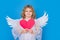 Angel kid with heart. Portrait of cute kid with angel wings isolated on studio background. Little angel, valentines day