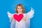 Angel kid with heart. Valentine's day. Blonde cute child with angel wings on a blue isolated studio background