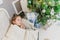 Angelic child daughter is sleeping on the sofa near Christmas tree with gifts.