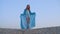 Angelic girl in waving blue tunic in sandy desert on clear sky landscape. Happy teen girl in blue tunic on sandy dune in