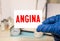 Angina word written on medical blue folder with patient files, pills and stethoscope on background