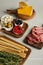 Angle view of boards with breadsticks, rosemary, salami slices, cheese and antipasto ingredients on white