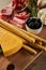 Angle view of cheese, breadsticks, salami slices, rosemary and bowls with antipasto ingredients on board on brown