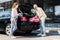 Angle view of happy man putting pink luggage in car trunk near woman