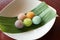 Angle view of Thai dessert flower shape stuff with crushed soybean and taro on wood table with banana leaf and white dish. Thai