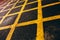 Angled closeup shot of a yellow, painted, grid road mark on black asphalt