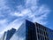 Angled view of a large, window covered building corner against a blue, cloud filled sky