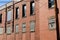 Angled view of old red brick industrial building, lower windows filled with glass block, interesting architectural details