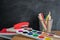 Angled view over a wooden desk with school supplies on it. Stepler, colored pencils, notebooks, calculator, scissors, tapes, paint