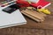 Angled view over a wooden desk with school supplies on it. Stepler, colored pencils, notebooks, calculator, scissors, tapes, paint